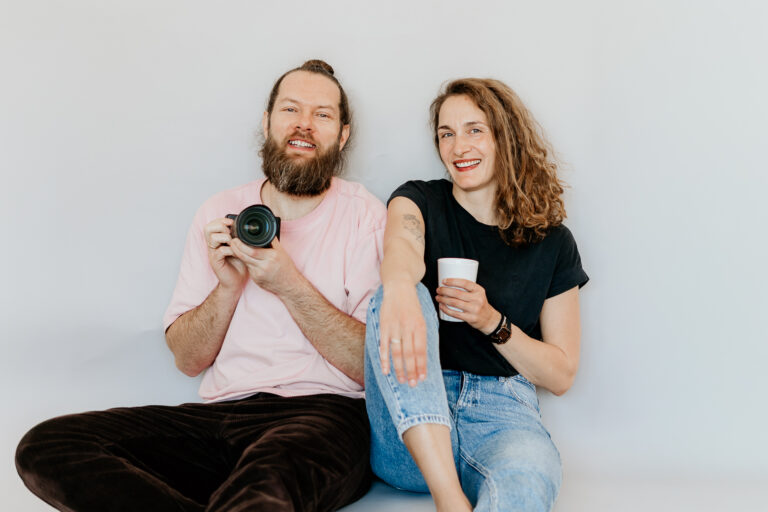 Als Fotograf ein Gewerbe anmelden. 2 Fotografen sitzen auf dem Boden und halten eine Kamera fest